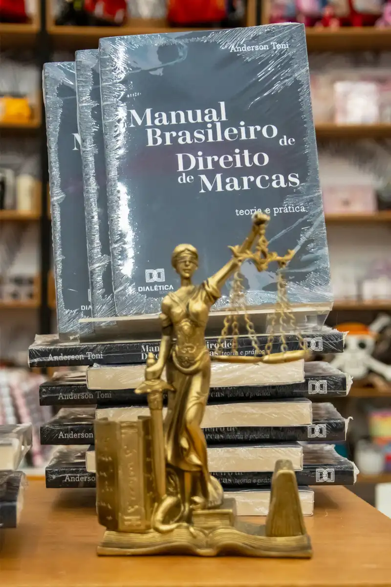 Exemplar do Manual Brasileiro de Direito de Marcas ao lado da Estátua da Justiça, simbolizando a doutrina técnica aplicada pela Densos.